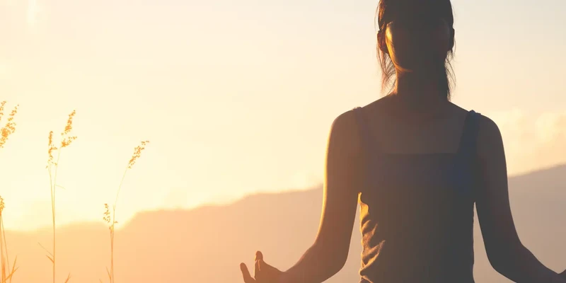 Person practicing meditation outdoors at sunset, representing mental wellness, mindfulness, emotional balance, and self-care during Mental Wellness Month.