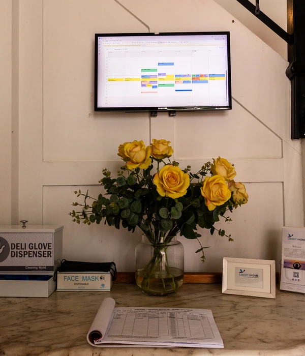 A marble reception desk featuring a vase of yellow roses, a visitor log, and a digital schedule display on the wall.