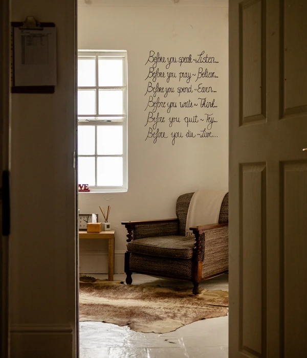 Cozy therapy room with an armchair and a wall decal featuring inspirational quotes beside a bright window.