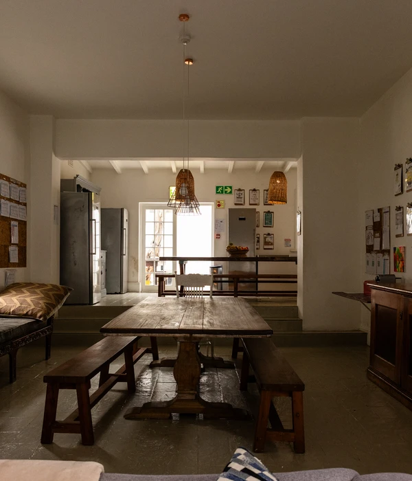 Rustic wooden dining area in a rehab center with long benches, a large table, and a bright kitchen in the background.