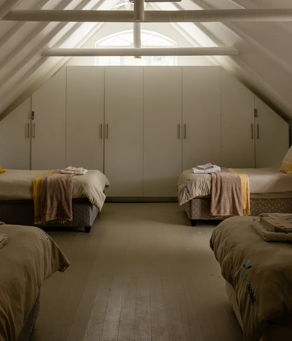 Spacious attic bedroom with several neatly made beds, white wardrobes, and vaulted ceilings with exposed white beams.